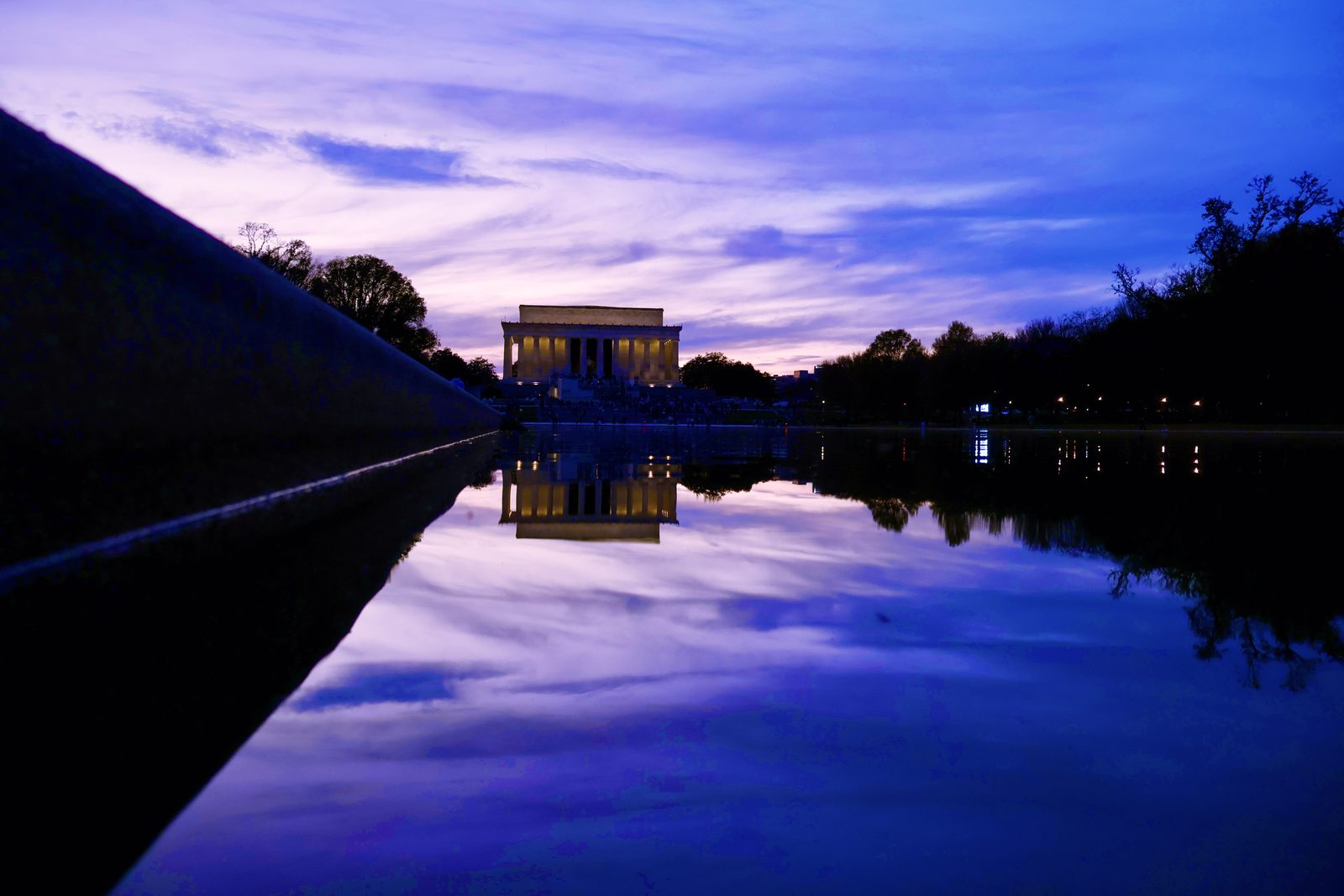 The Lincoln Memorial glowing across the still reflecting pool at blue hour, an angled wall slicing the frame.