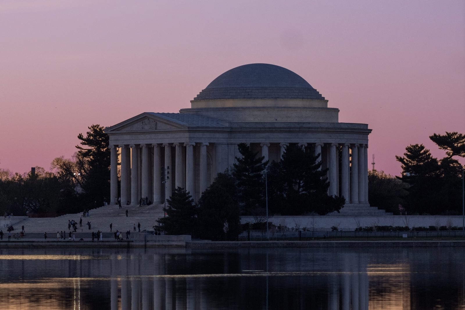 The Jefferson Memorial silhouetted against a pink-orange sunset, reflected in the Tidal Basin.