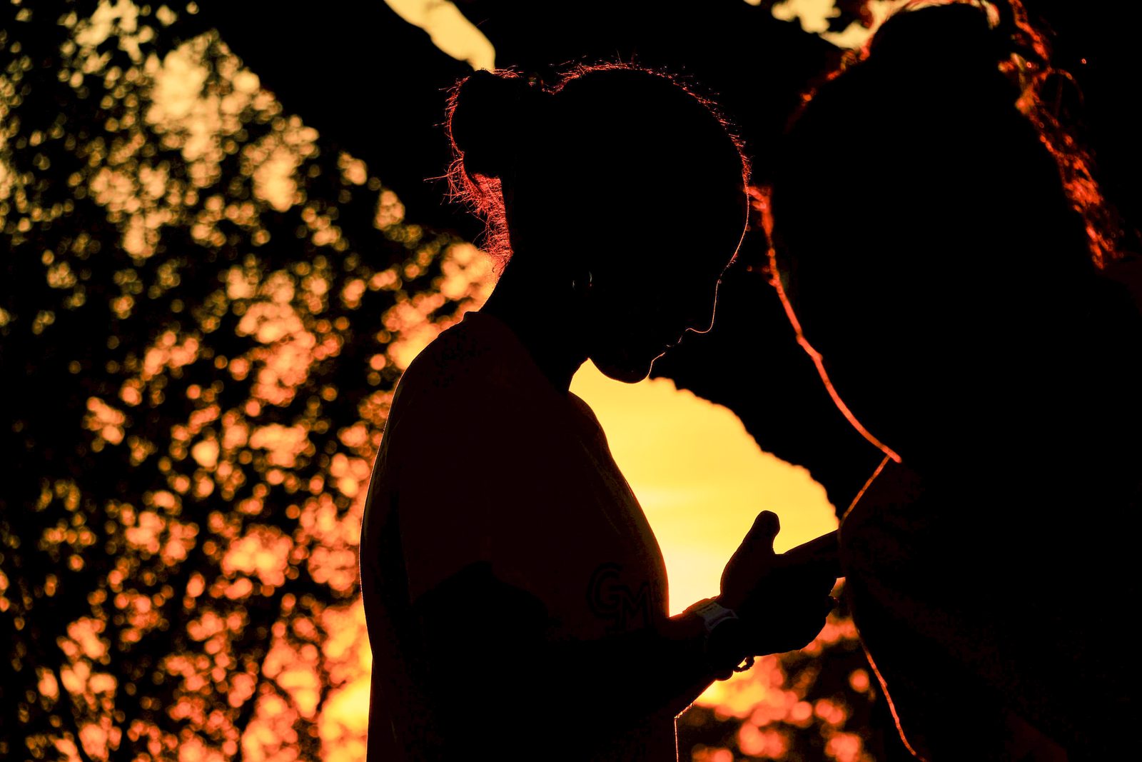 Backlit silhouette portrait of a person at golden hour, glowing bokeh foliage and sun flare behind them.