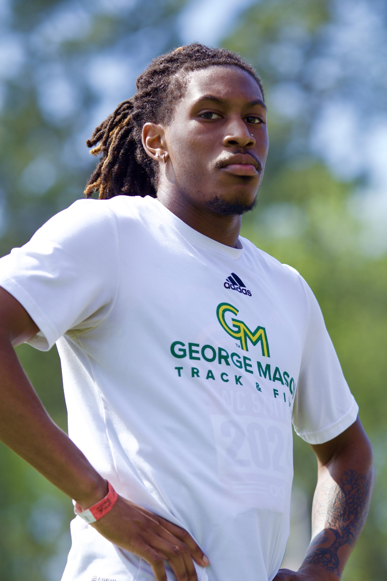 Portrait of a George Mason track-and-field athlete in a white team T-shirt, mid-day light.