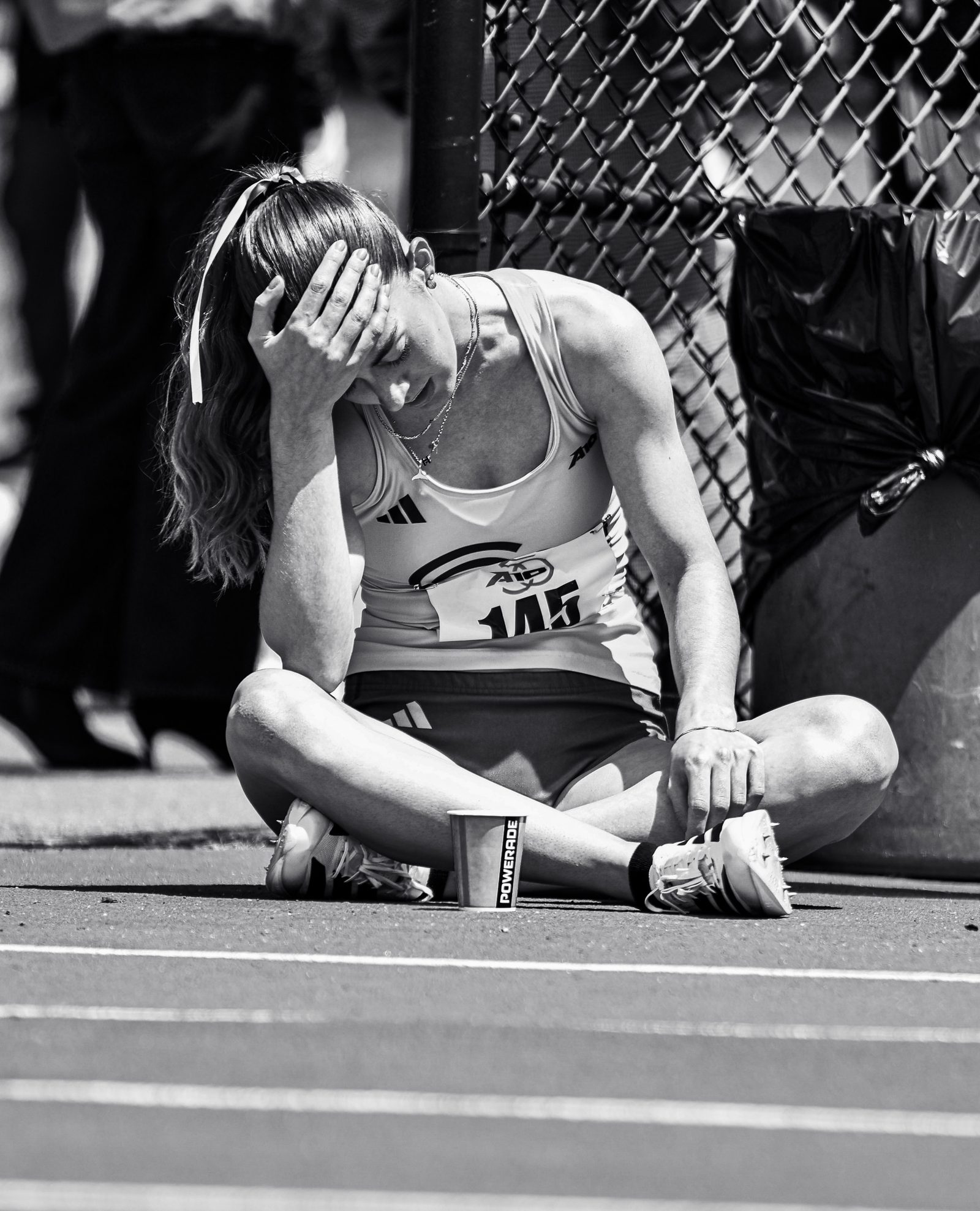Black-and-white portrait of a track athlete sitting on the track after a race, head in hand.