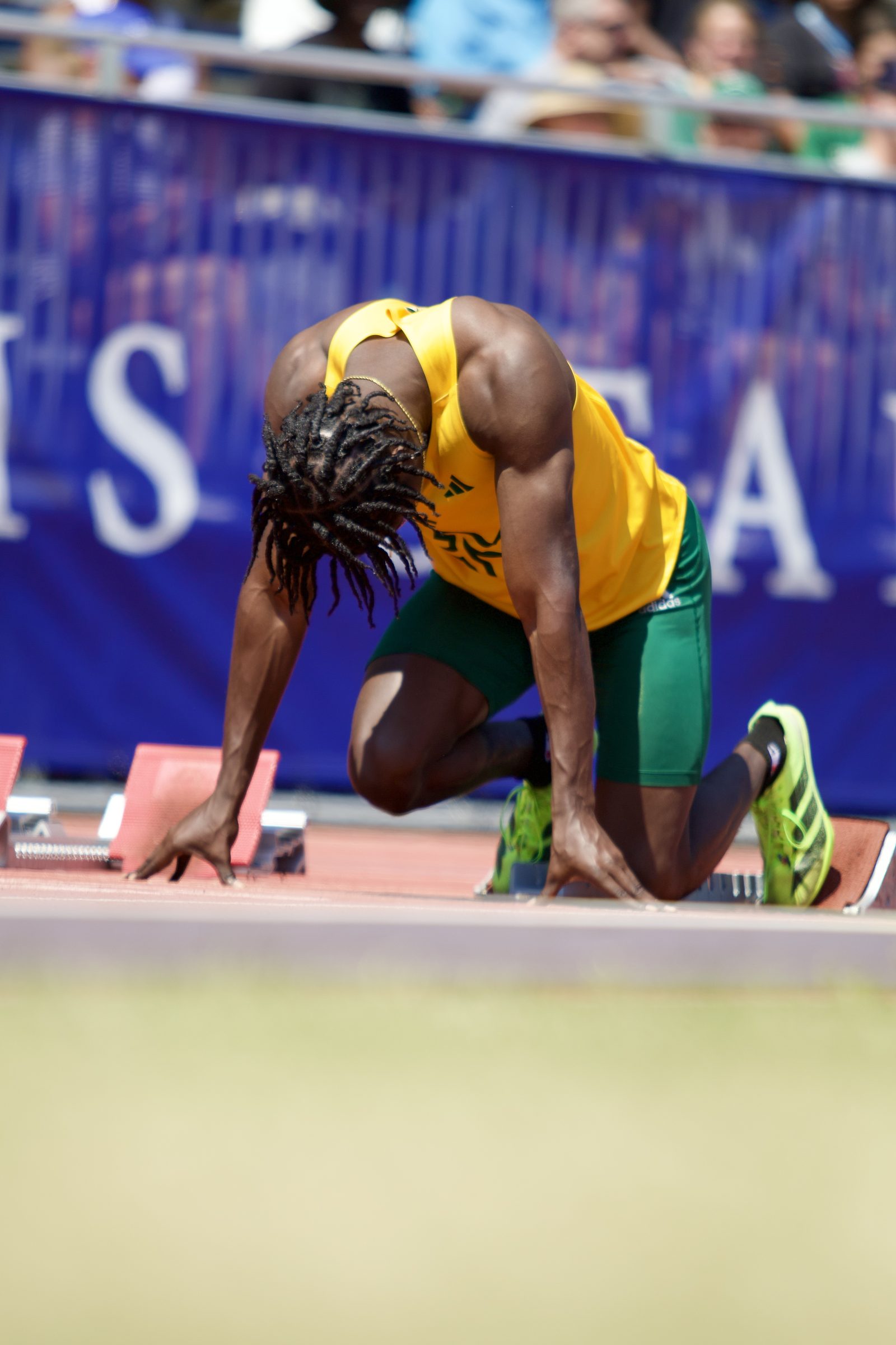Sprinter in a yellow uniform set in the starting blocks, head down before the gun.