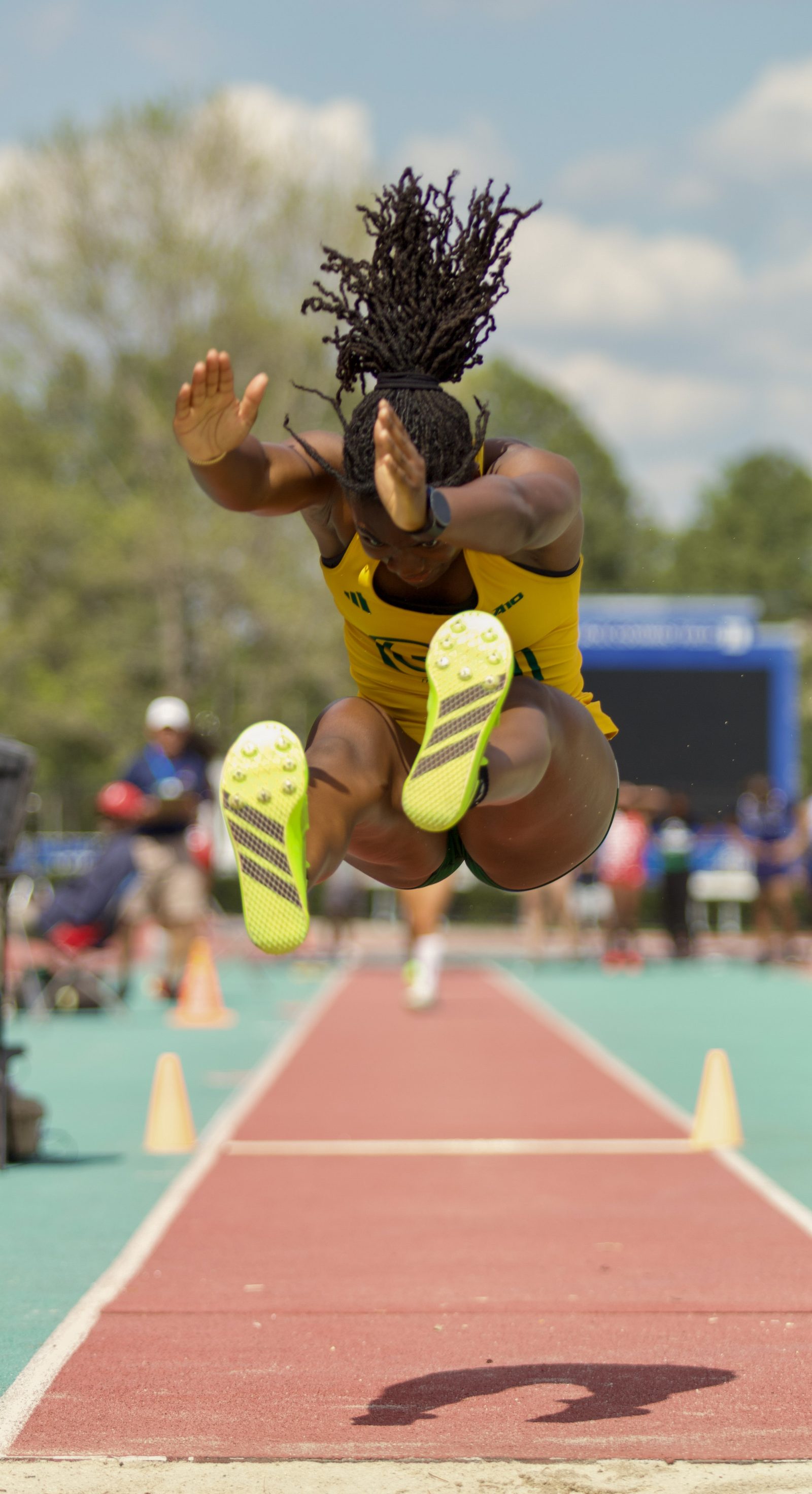 Long jumper airborne over a long-jump runway, neon-yellow spikes visible.