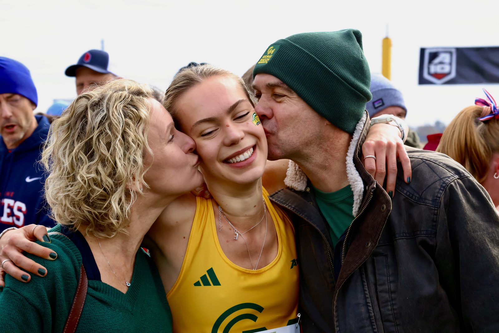 A track athlete being kissed on both cheeks by her parents in the crowd after a championship meet.