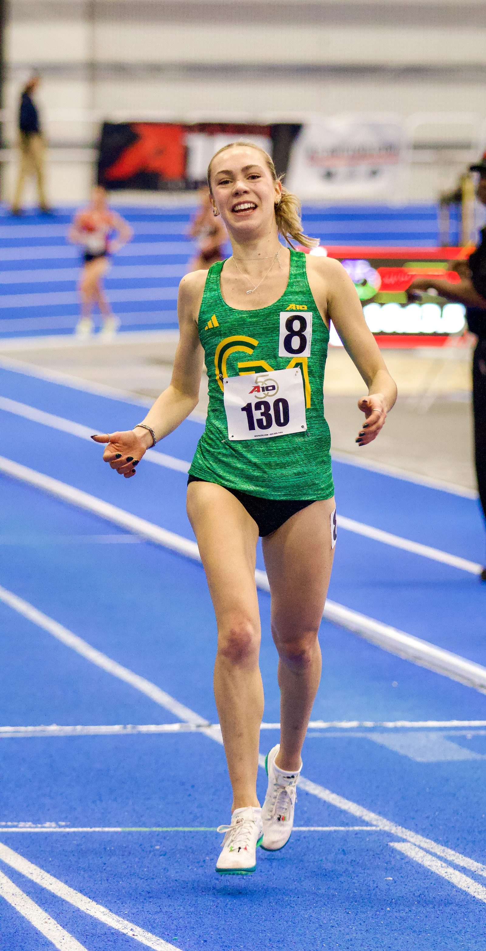 George Mason distance runner crossing the finish line, smiling and looking up.