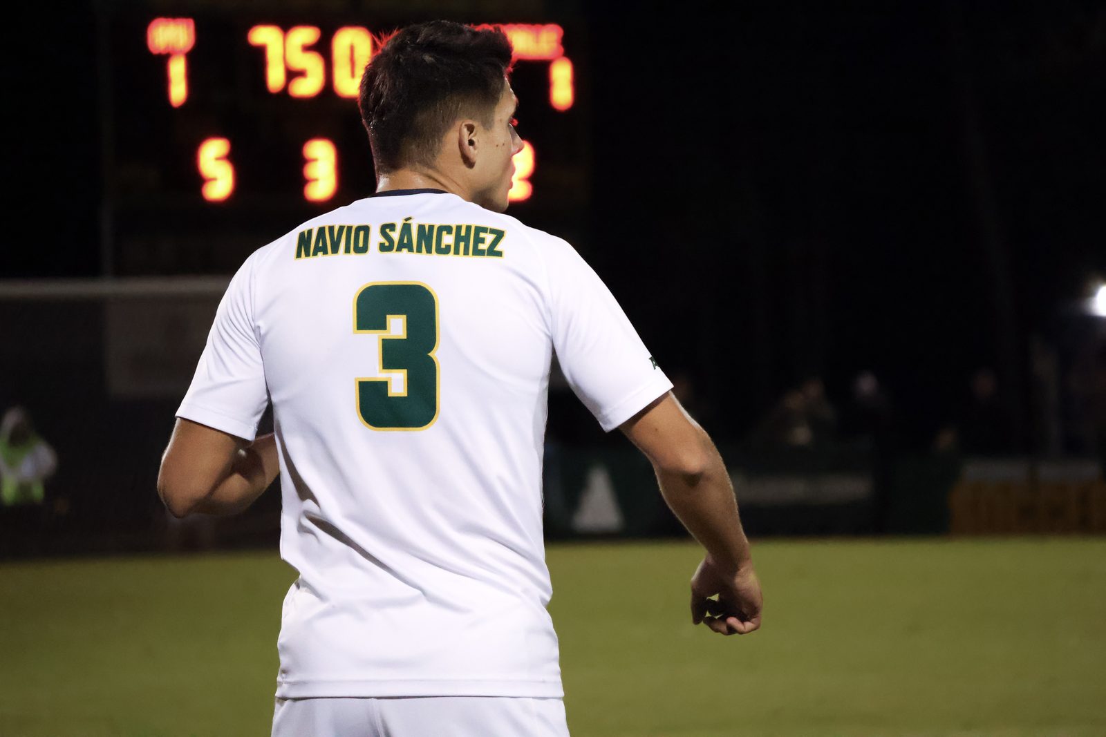 Soccer player number 3, Navio Sánchez, photographed from behind with stadium scoreboard in the background.